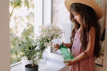 happy kid girl taking care of houseplants at home, dressed in stylish dusty pink outfit. the concept of home gardening. High quality photo