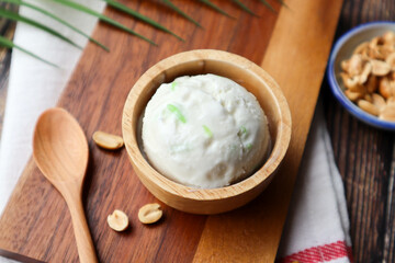 Scoop of coconut milk ice cream in wood bowl  with peanuts topping on the side - Top view of Thai famous dessert