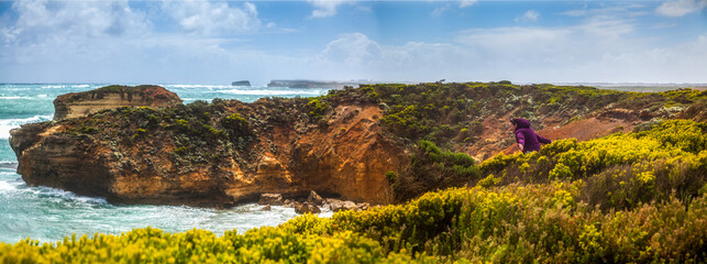 Panorama of rock coast, where happy girl walks between thickets looking at ocean