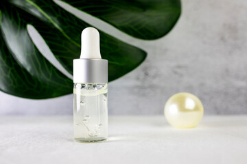 Dropper bottle with a transparent gel-like liquid inside on the background of a green plant. Side view, place for text.