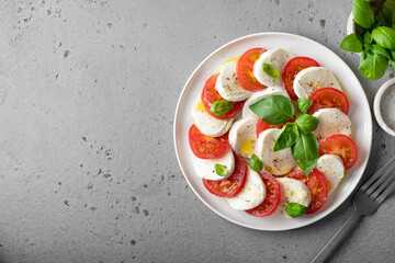 Italian caprese salad with sliced tomatoes, mozzarella, basil, olive oil on a gray background. Top view, place for text.