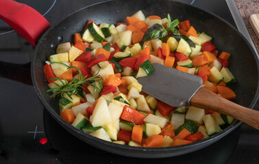Black pan full of small pieces of potatoes, pepper, zucchini and carrots to prepare a healthy vegetable dish. Wellness and diet with vegetables.