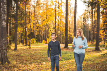 A beautiful mother and teenage son walk together in the autumn park. Happy family. Family weekend.