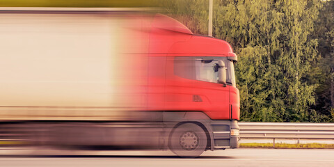 A heavy truck is driving on the motorway. Motion blur, soft focus. Panoramic image.