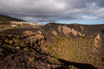 Mouth of one of the volcanoes, with lava and pine trees inside and behind a town, before eruption in Cumbre Vieja Natural Park, Canary Islands, Spain