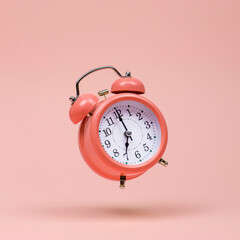 The pink alarm clock is levitate in the air, against a pink background. The concept of time, copy...