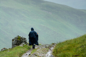 Along the West Highland Way. A lonesome hiker protected by a rain cape walks on the hiking path...