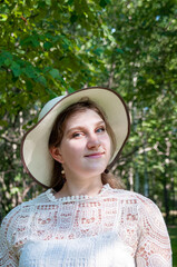 Portrait of a beautiful girl in a hat in summer on the background of a green forest