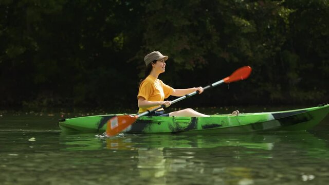 Happy young woman rowing in green kayak to the river bank. Real time. The concept of kayaking