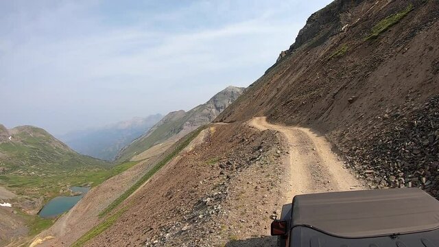 Rooftop view of driving on Black Bear Pass trail cut into a steep and rock mountainside high above Ingram Lake near Telluride Colorado; concepts of adventure, danger, and exploration