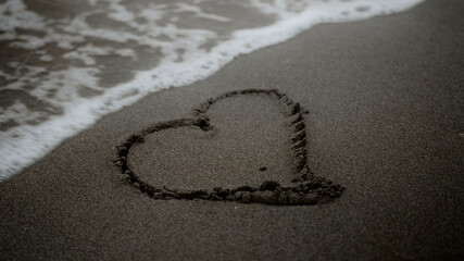 The symbol of heart drawn on a beach, sea wave erase it, metaphor of love and separation
