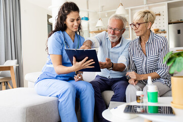 Female nurse talking to seniors patients while being in a home visit, senior couple signs an...