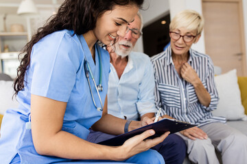 Female nurse talking to seniors patients while being in a home visit, senior couple signs an insurance policy.