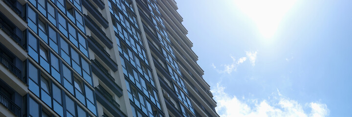 Multi-storey building with many glass windows standing against background of blue sky and sun