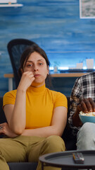 POV of interracial couple watching movie on TV with snack at home. Married multi ethnic lovers looking at camera while eating popcorn in living room. Mixed race people bonding on sofa