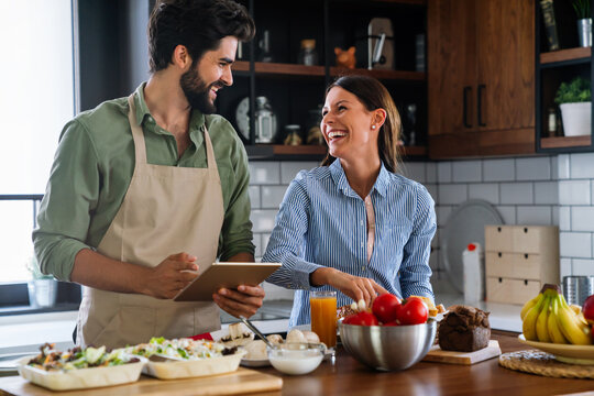 Beautiful young couple is using a digital tablet and smiling while cooking in kitchen at home