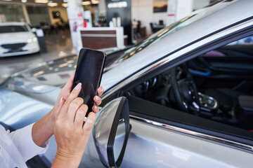 Person with modern gadget standing in car showroom
