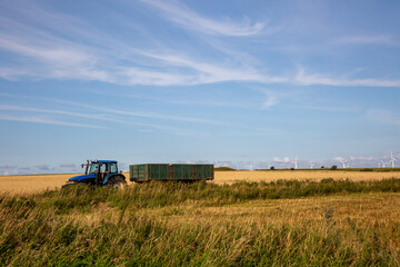 Fototapeta premium Ein Traktor mit Anhänger fährt über ein Feld