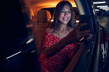 Joyful woman sitting in automobile and using smartphone