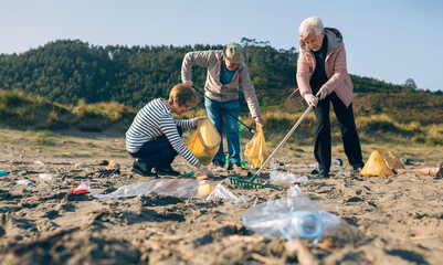 Group of senior volunteers picking up trash on the beach. Selective focus on people in background