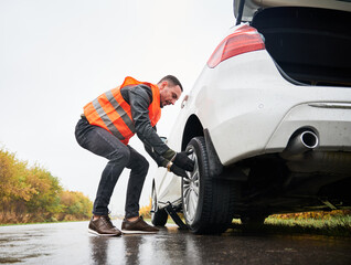 Roadside assistance worker removing flat tire while repairing car on the street. Male auto mechanic...