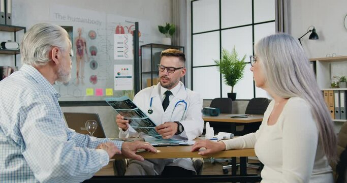 Attending physician in glasses checking x-ray of aged male, giving consultation and treatment. has Caucasian man is listens to the diagnosis, wife positive support him