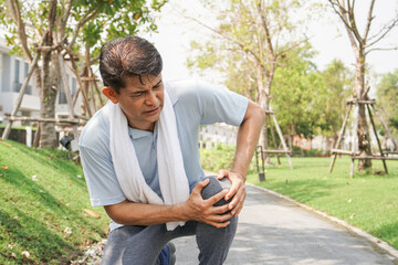 Asian senior man falling down and getting knee hurt from walking or jogging exercise at the park....