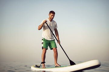 Young man in t-shirt and shorts floating on SUP board