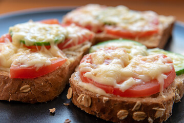 Hot sandwiches with mayonnaise, tomatoes, cucumber and grated cheese on a black plate