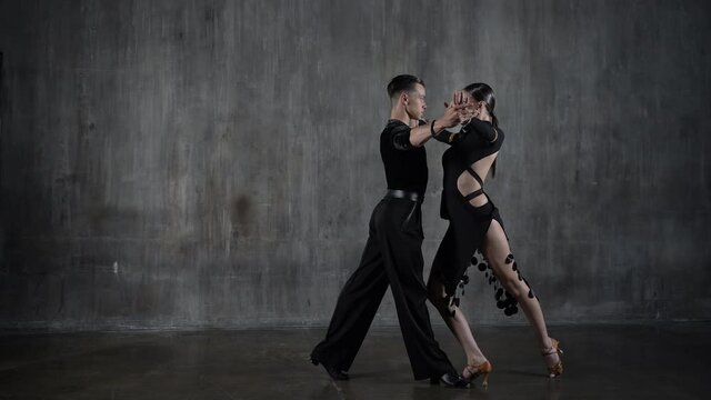 The young dance ballroom couple in black dress dancing in sensual pose on studio background. Professional dancers dancing latino. Ballroom dance concept. Human emotions - love and passion