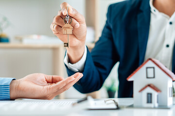 Real Estate Broker Or businessman holding white house model and house key in hand.Mortgage loan approval home loan and insurance concept.