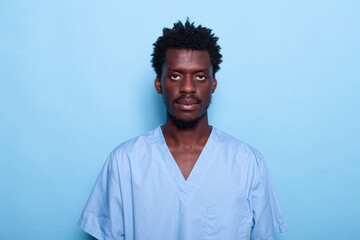 Portrait of black man nurse standing over blue background in studio. African american person working as medical specialist looking at camera and feeling confident. Adult in uniform