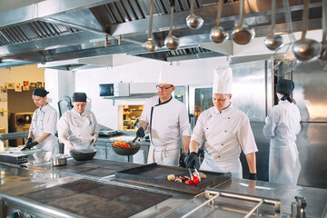 Five chefs wearing uniforms posing in a kitchen .
