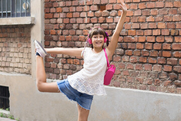 young smiling girl is dancing listening music in a city street