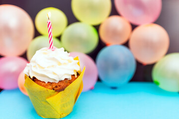 Birthday cupcake.Pastel yellow birthday cupcake with candle and blurred balloons.colorful birthday.Closeup,copy space.