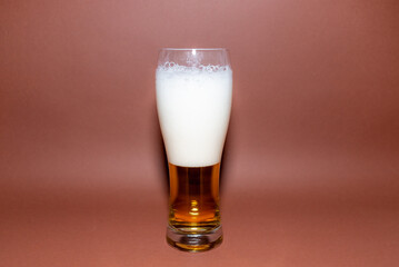 One Glass beer on brown background with copy space.Amber glass beer with foam. brown background.Selective focus.