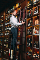 The seller of alcoholic beverages sorts bottles standing on the ladder.