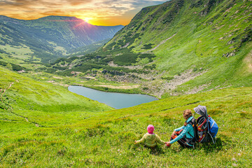 Fototapeta na wymiar Mom and daughter admire the sunset over Lake Brebeneskul in the Carpathians. Ukraine