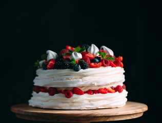 Fruit cake. Cake decorated with berries on a wooden stand on a black background.