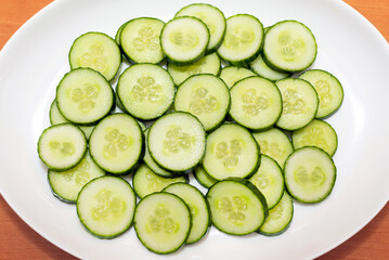 Sliced oval shape fresh cucumber Cucumis sativus in a white plate.Top view.