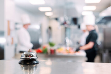 Table distribution in the restaurant. Cooks prepare food in the kitchen against the background of a metal bell.