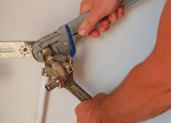 Replacement of the watering tap. The plumber uses an adjustable wrench to turn the watering tap. Close-up.