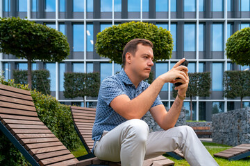 Business man checking e-mail. Handsome man using mobile phone in recreation area in front of business center. Urban lifestyle leisure concept. Guy texting on mobile phone in park. Man sitting on bench