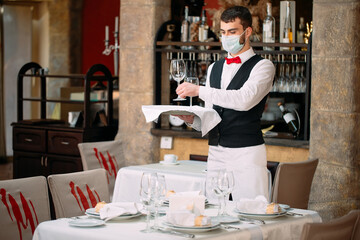 A waiter in a medical protective mask serves the table in the restaurant.