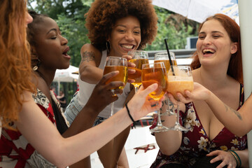 Cinematic shot of young happy girl friends of different ethnicities are having fun to drink cocktails during vacation at bar. Concept of friendship, lifestyle, youth, diversity, multiethnic, freedom.