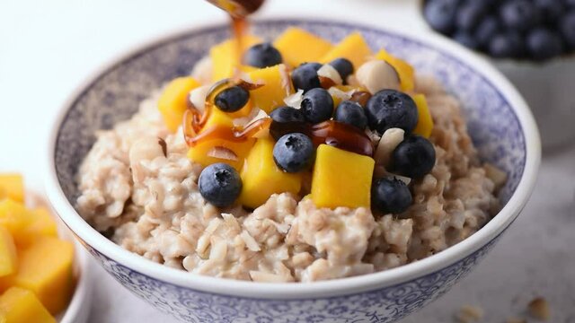 Honey pouring on oatmeal porridge bowl. Healthy breakfast cereals