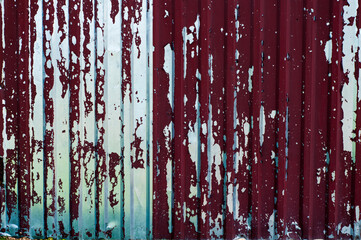 Damaged corrugated metal sheet, weathered rusted steel, grunge background with red painted metal, textured surface, outdoors
