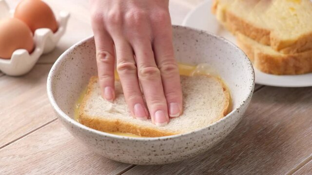 Soak slice of white toast bread in egg milk mixture to prepare french toast. Female hands cooking tasty healthy breakfast