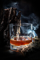 Whiskey, rum, or bourbon poured into a clear glass. Decorations in the style of wood and smoke around.