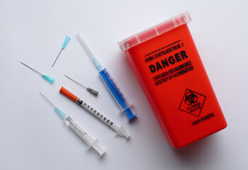 Disposable syringes with needles and sharps container on white background, top view